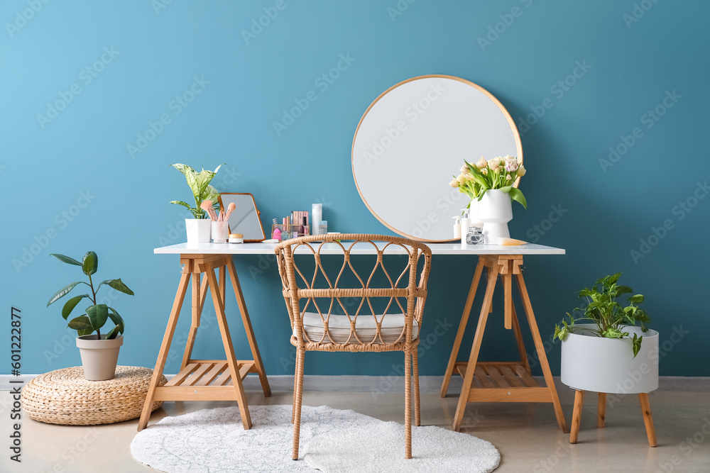 Table with different cosmetics and tulip flowers near blue wall