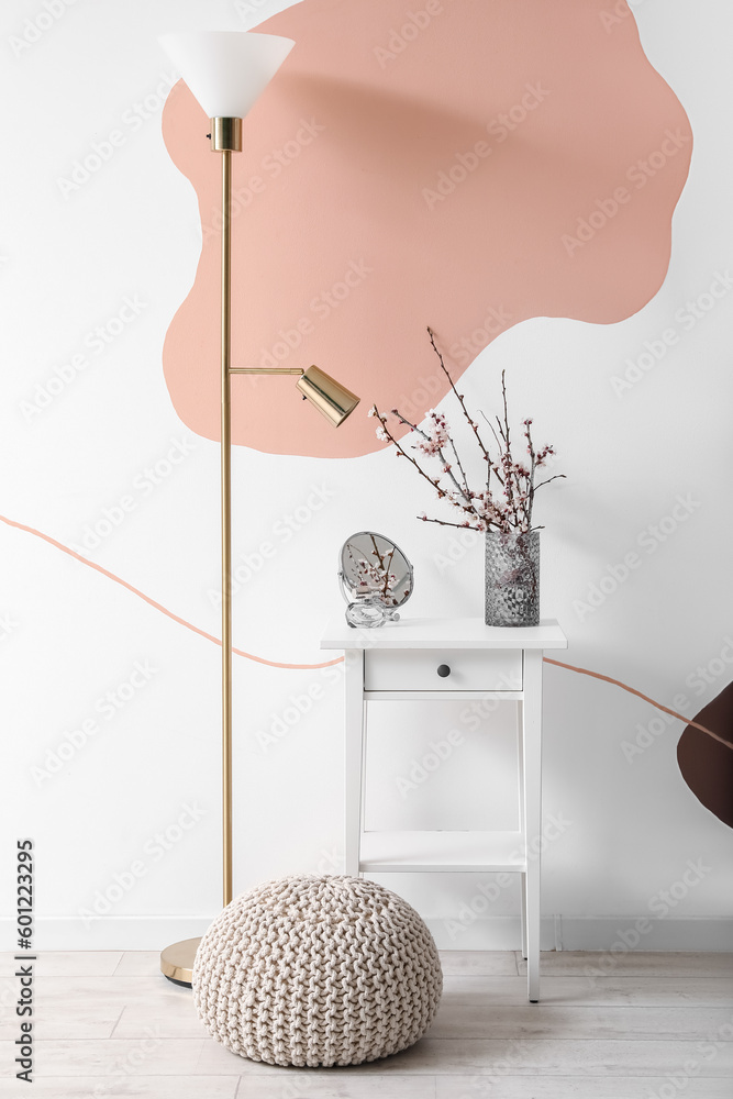 Vase with blooming branches, perfume and mirror on table in stylish room