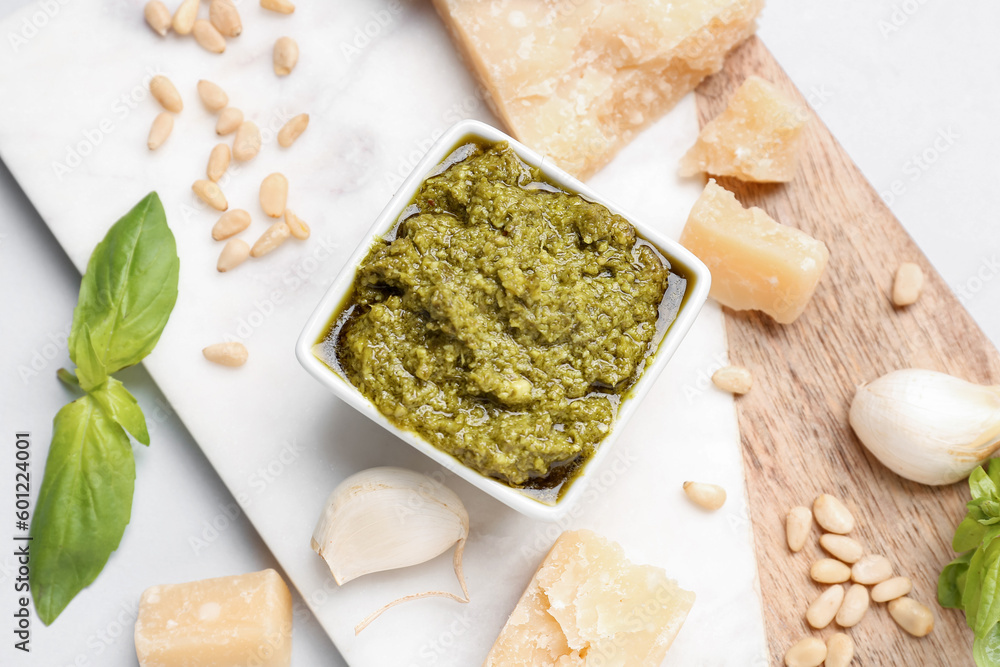 Board with bowl of delicious pesto sauce and ingredients, closeup