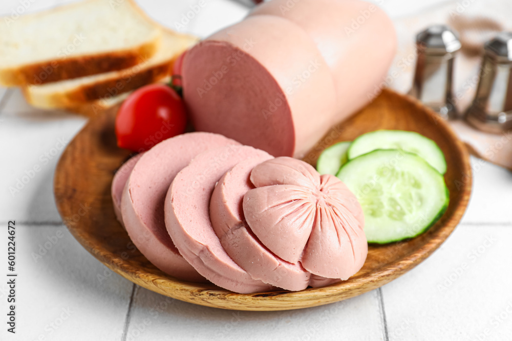 Plate with tasty sliced boiled sausage on white tile background, closeup