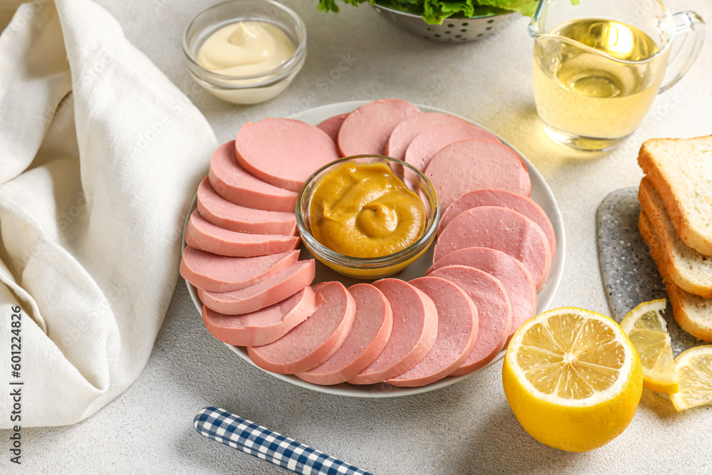 Plate with tasty sliced boiled sausage and sauce on light background