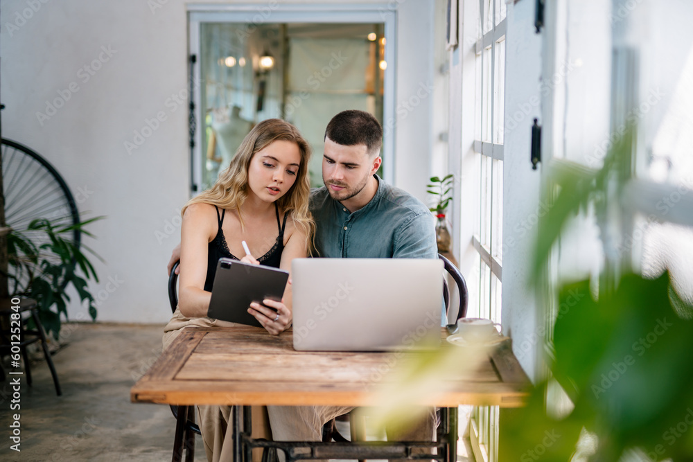 Young couple sit at table looking at laptop screen, buying goods, tickets online. The concept of cou