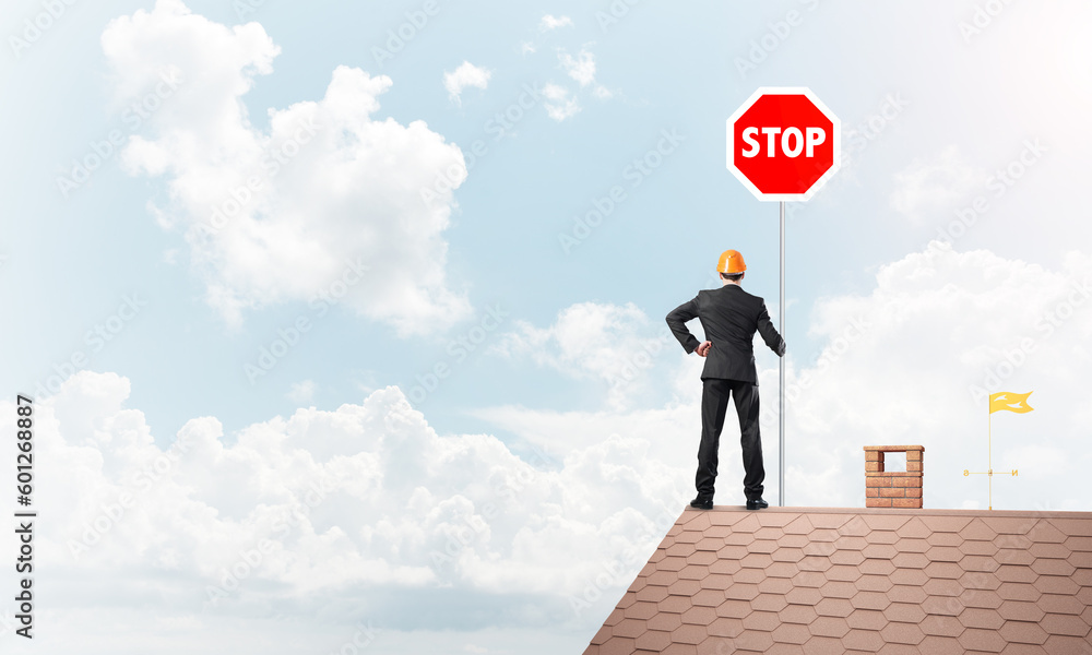 Caucasian businessman on brick house roof showing stop road sign. Mixed media