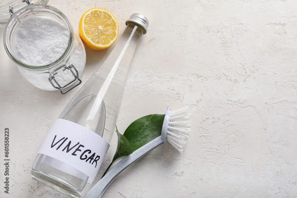 Bottle of vinegar, baking soda, brush and lemon on light background