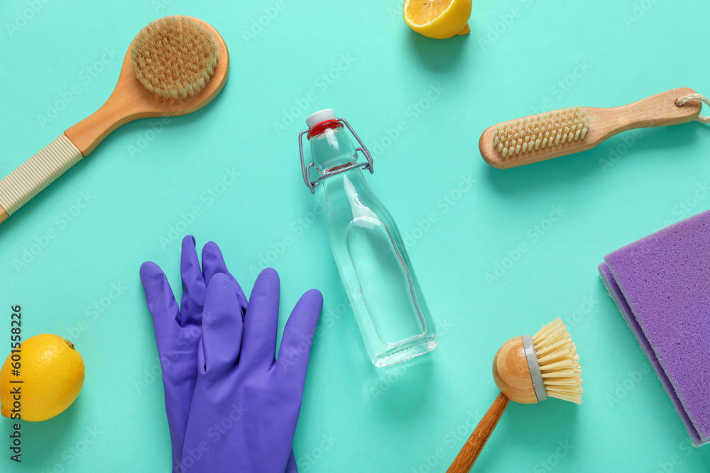 Bottle of vinegar, rubber gloves, brushes, sponge and lemons on color background