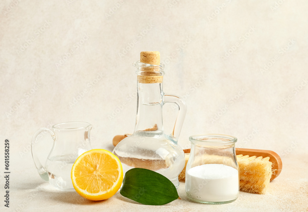 Jugs of vinegar, baking soda, brush and lemon on light background