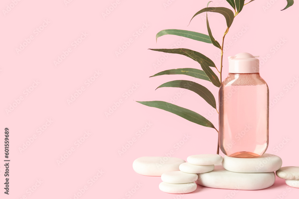 Bottle of micellar water with plant branch and spa stones on pink background