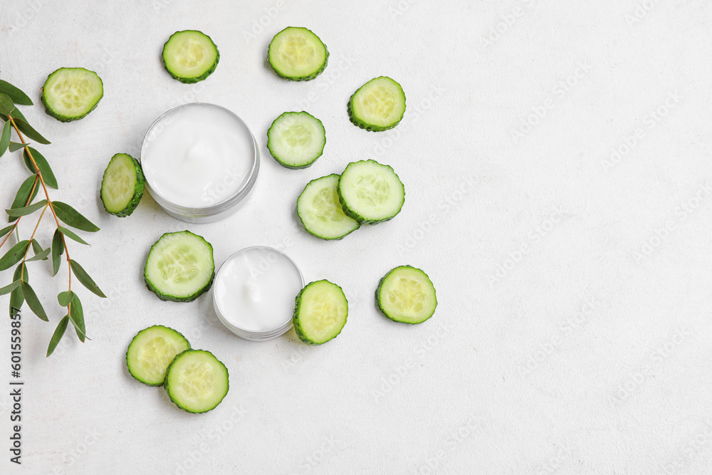 Composition with jars of natural cream, cucumber slices and eucalyptus branch on light background