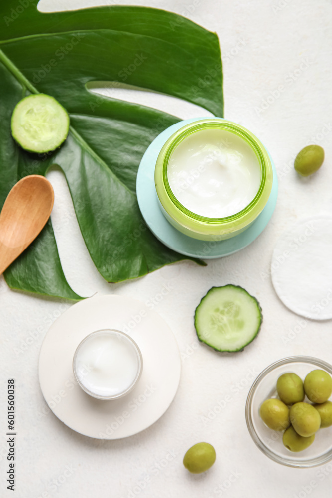 Composition with jars of natural cream, ingredients and palm leaf on light background