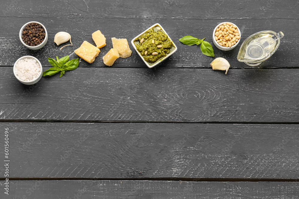 Composition with bowl of pesto sauce and ingredients on black wooden table