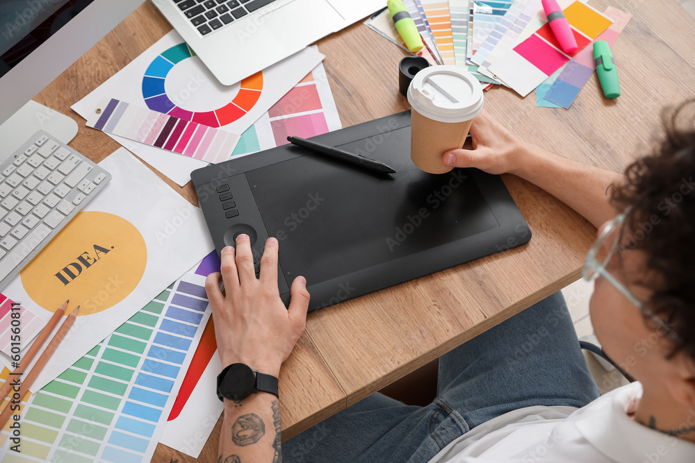 Male graphic designer with cup of coffee working at table in office, closeup