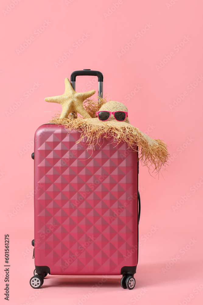 Suitcase with straw hat, sunglasses and starfish on pink background