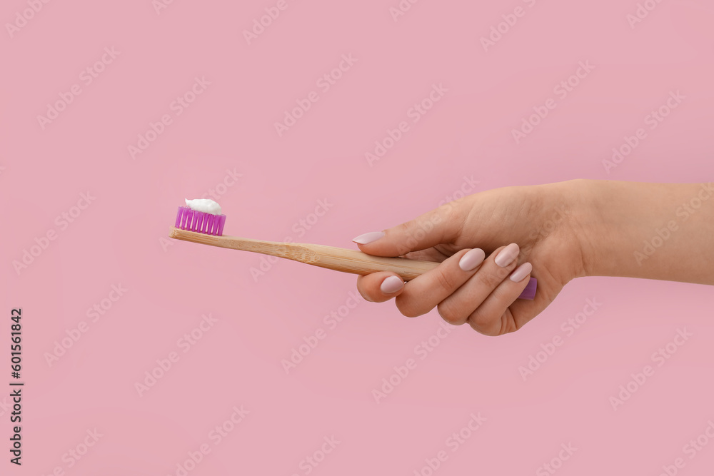 Female hand with toothbrush and paste on pink background