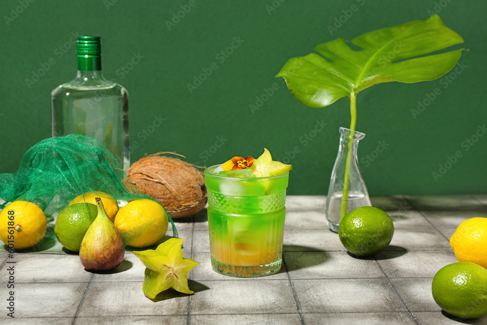 Fresh summer cocktail with carambola and flower on tile table near green wall