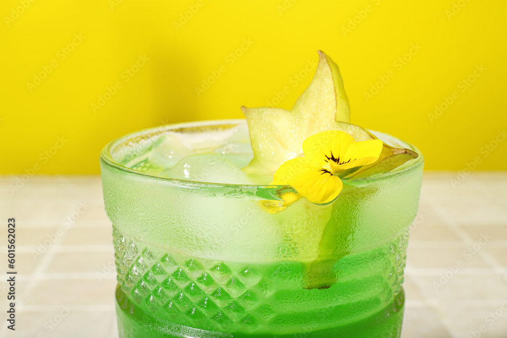 Fresh summer cocktail with carambola on tile table near yellow wall