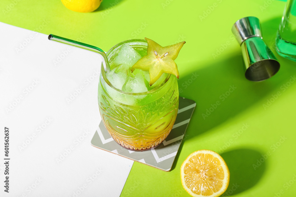 Fresh summer cocktail with carambola and straw on green table