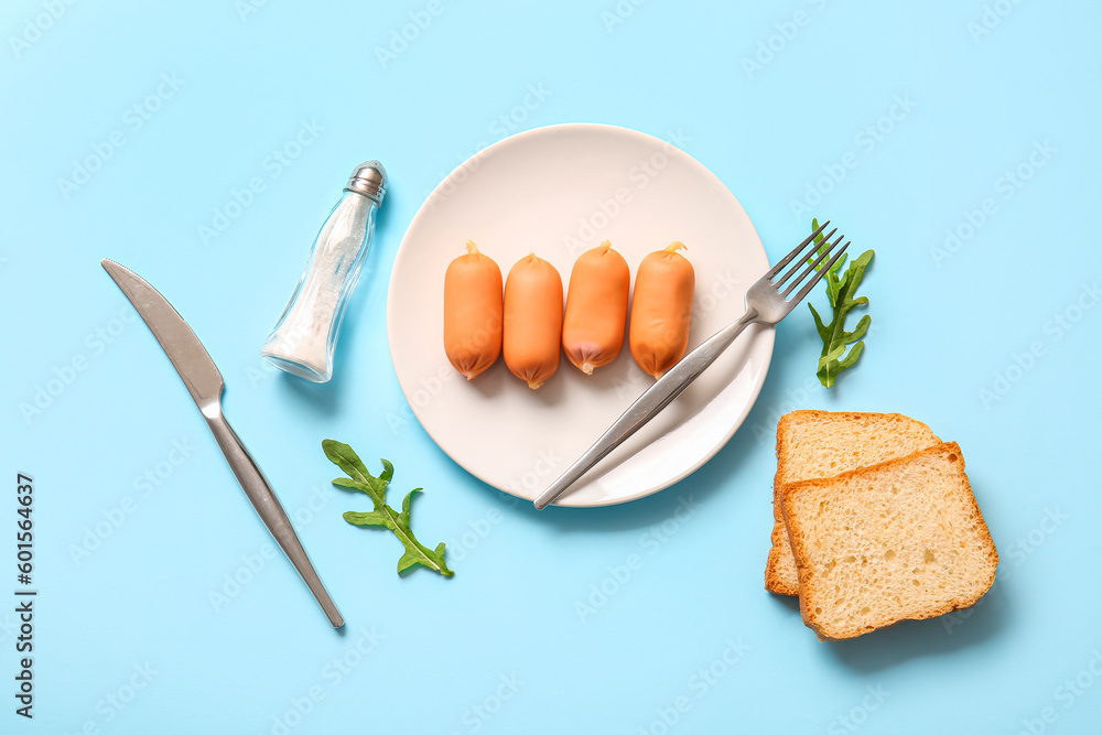 Plate of tasty boiled sausages with bread and arugula on blue background