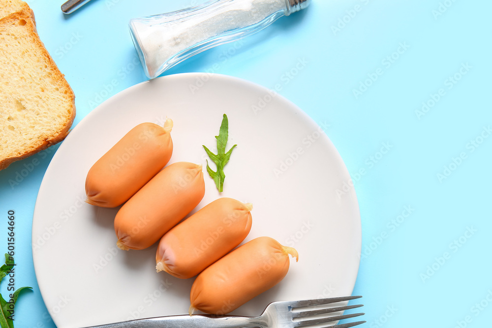 Plate of tasty boiled sausages with bread and arugula on blue background