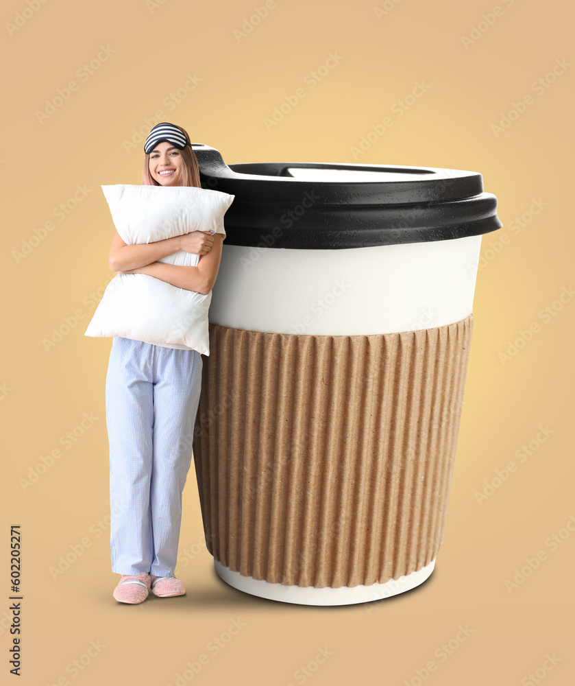 Portrait of young woman with pillow and big cup of coffee on beige background