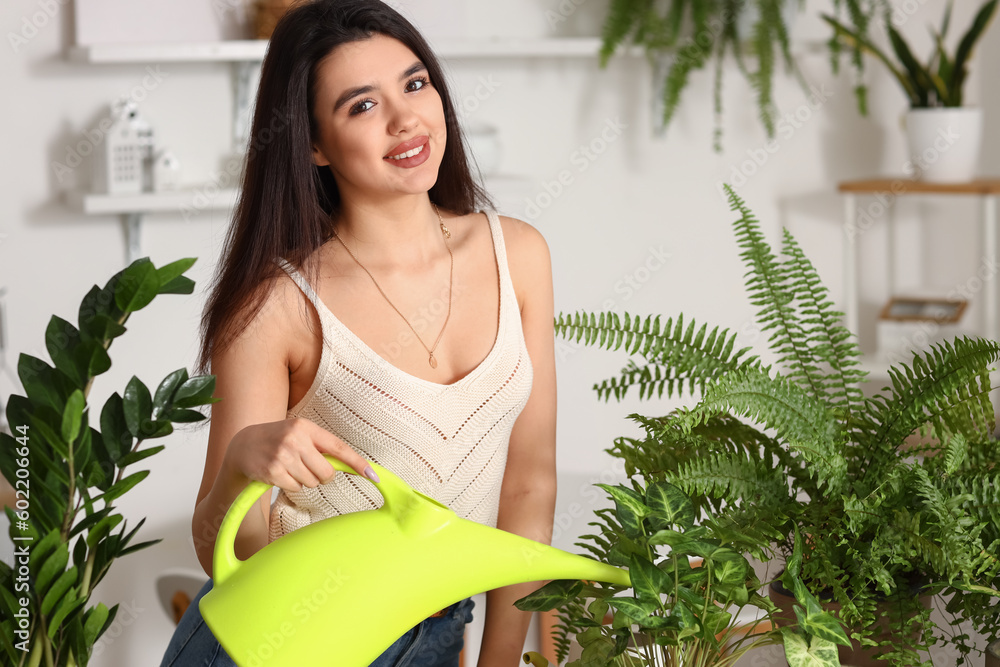 Young woman watering green houseplant in kitchen