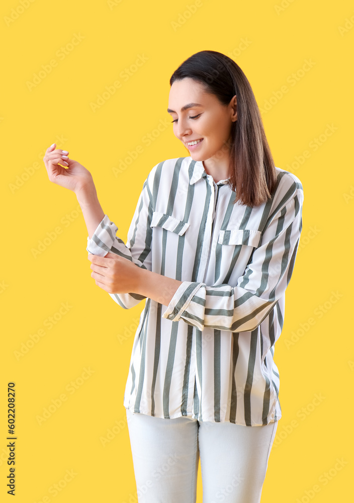 Beautiful young woman rolling up her sleeve on yellow background