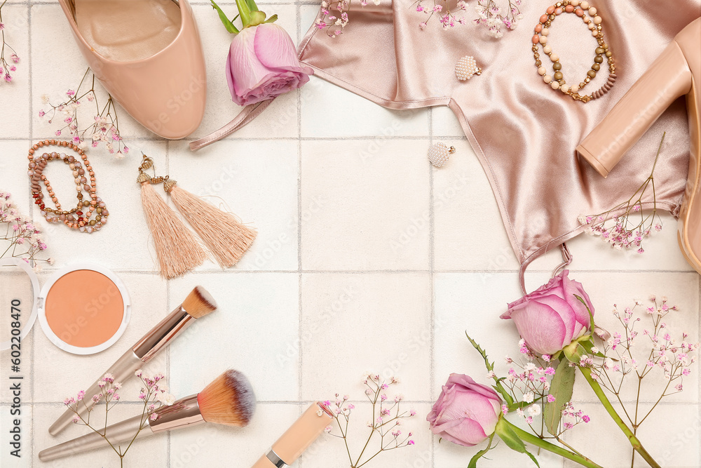 Frame made of female accessories, cosmetics, clothes and flowers on light tile background