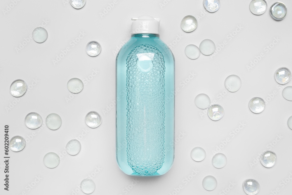 Bottle of micellar water with glass stones on light background