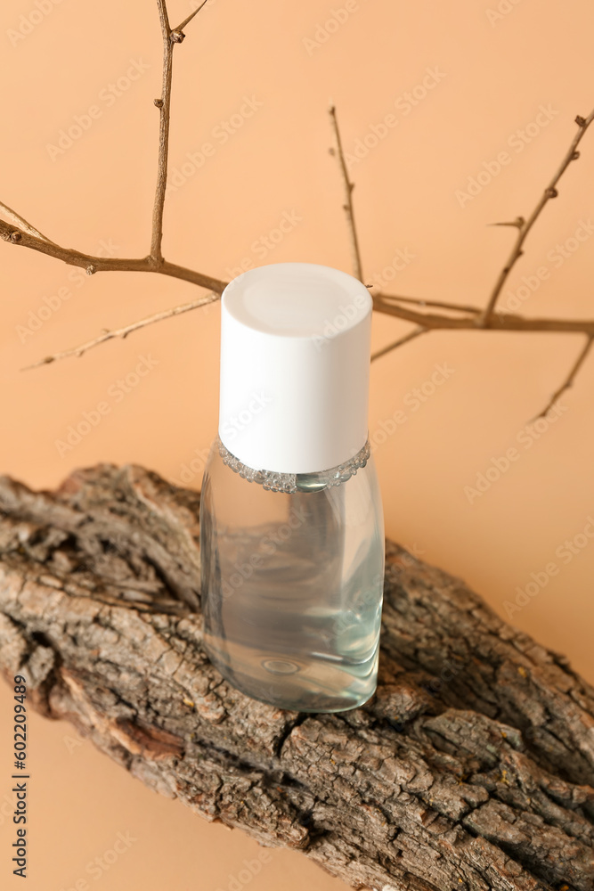 Bottle of micellar water with tree branch and bark on beige background, closeup