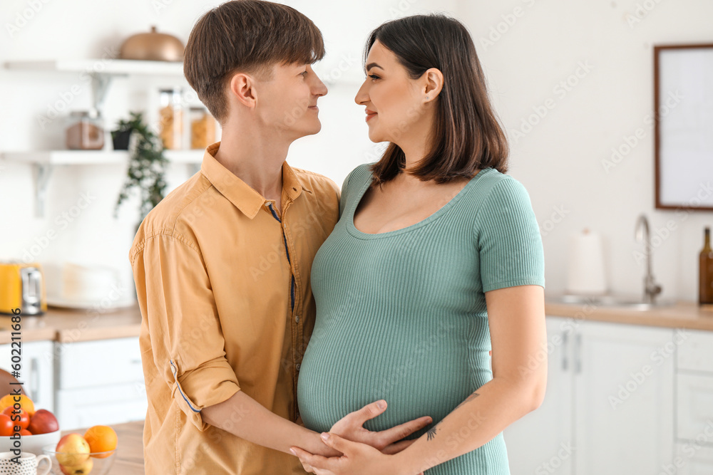 Young pregnant couple hugging in kitchen