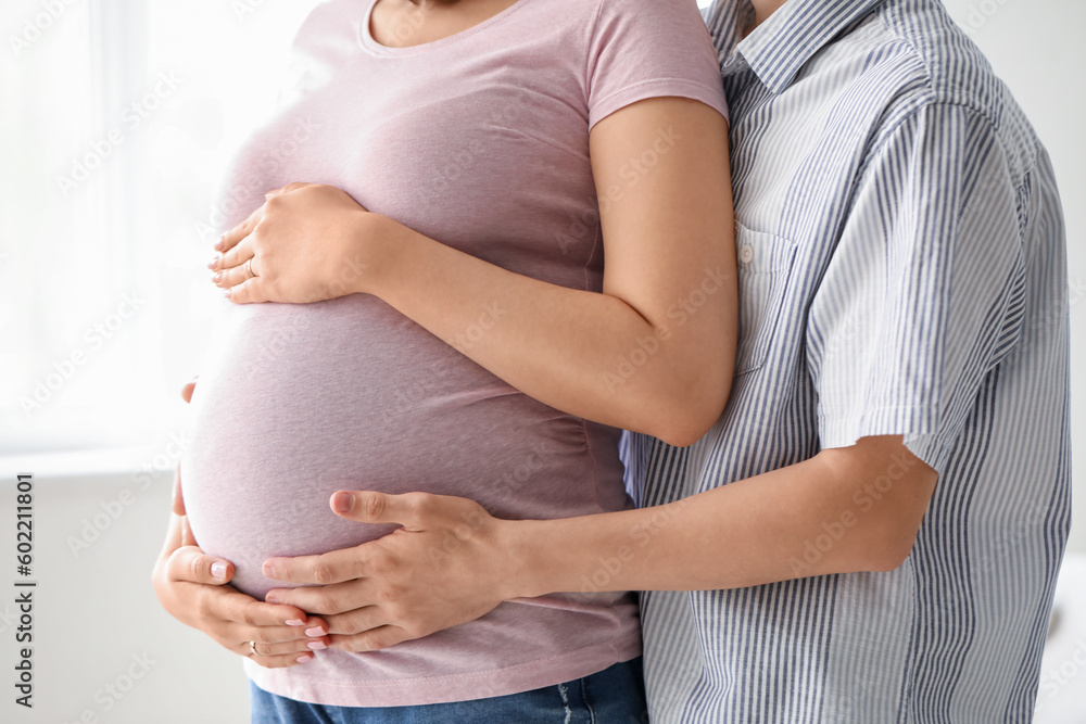 Young pregnant couple hugging at home, closeup