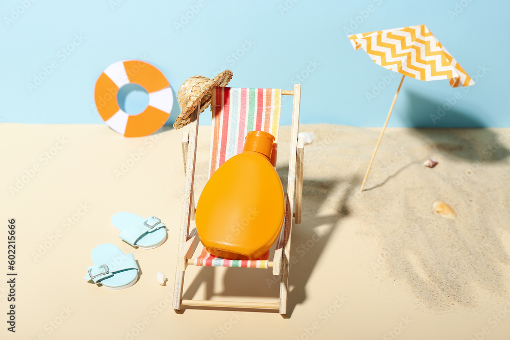 Creative composition with miniature deckchair, umbrella and sunscreen on beach