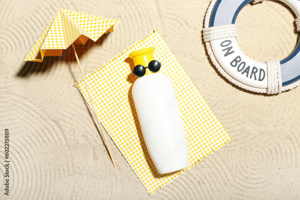 Creative composition with sunscreen, miniature umbrella and lifeline on sand