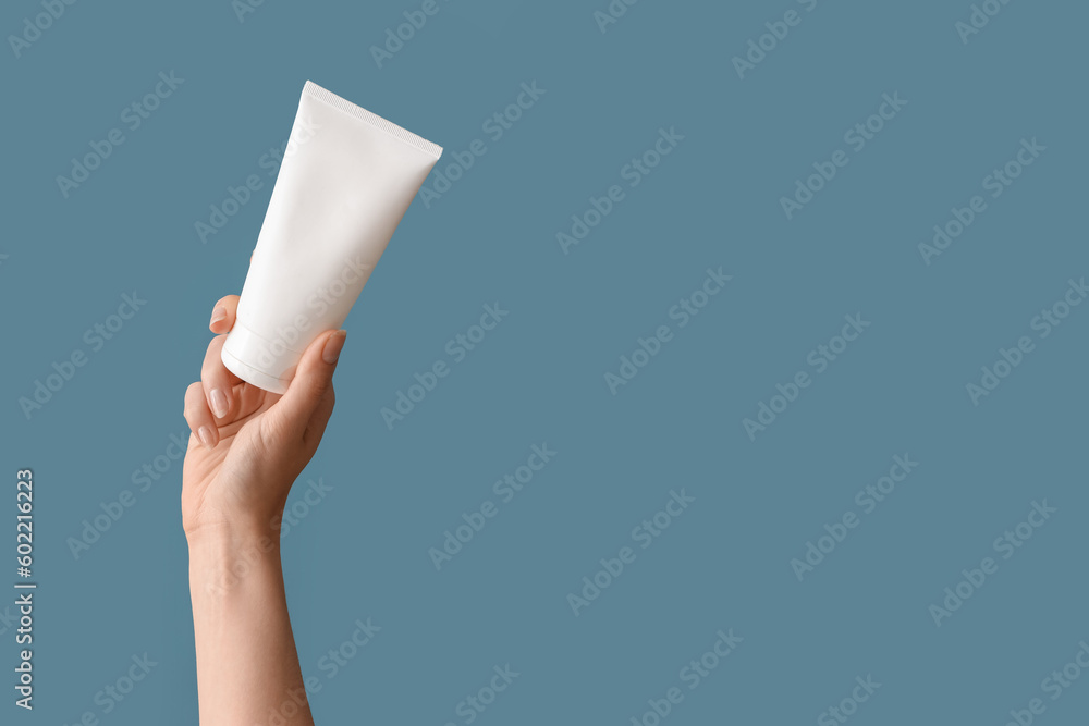 Hand holding tube with cosmetic product on blue background