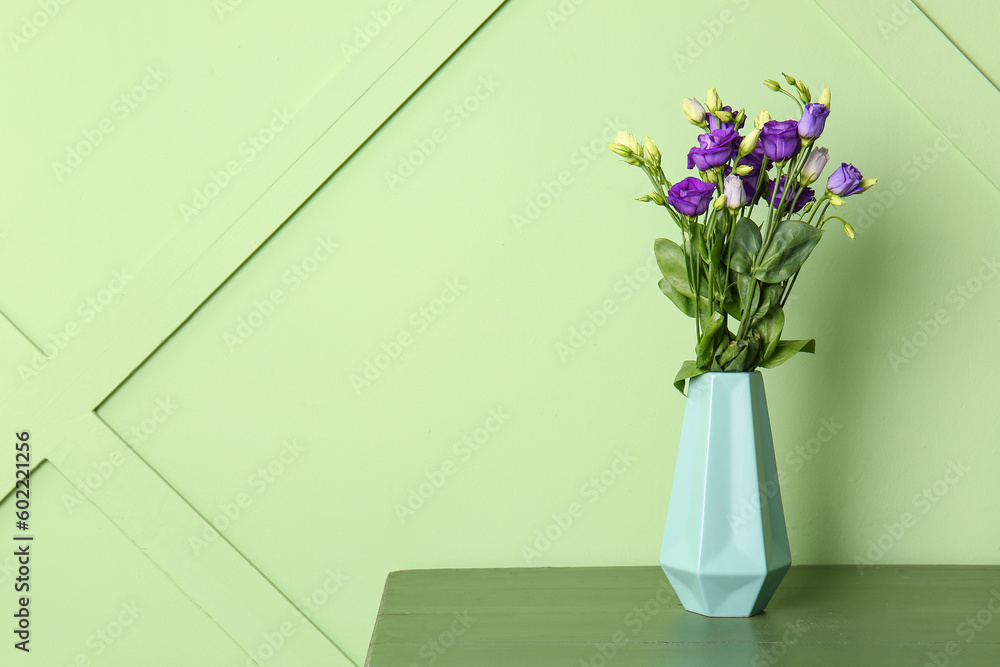 Vase with eustoma flowers on table near green wall