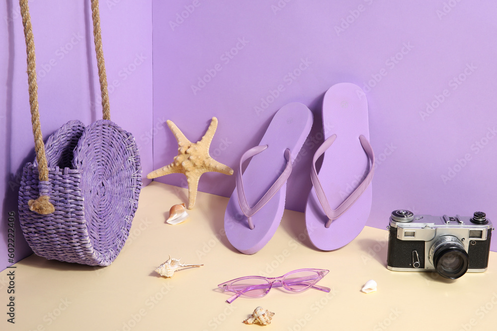 Flip flops with sunglasses, camera and bag on lilac background