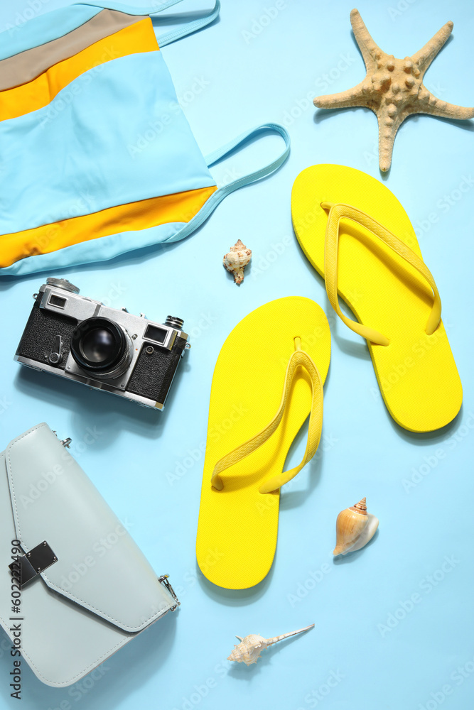 Flip flops with swimsuit, camera and bag on pale blue background