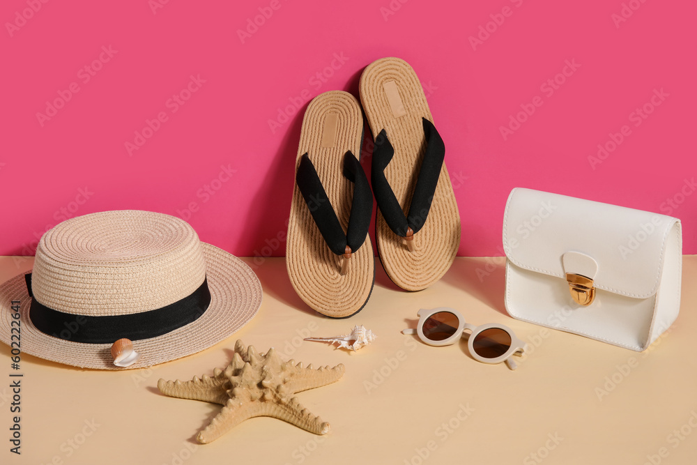 Flip flops with sunglasses, bag and wicker hat near pink wall