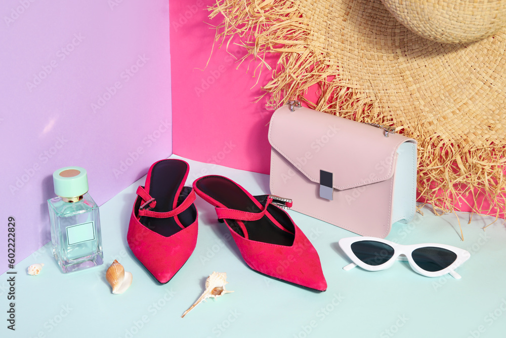 Pair of sandals with sunglasses, bag and wicker hat near color wall