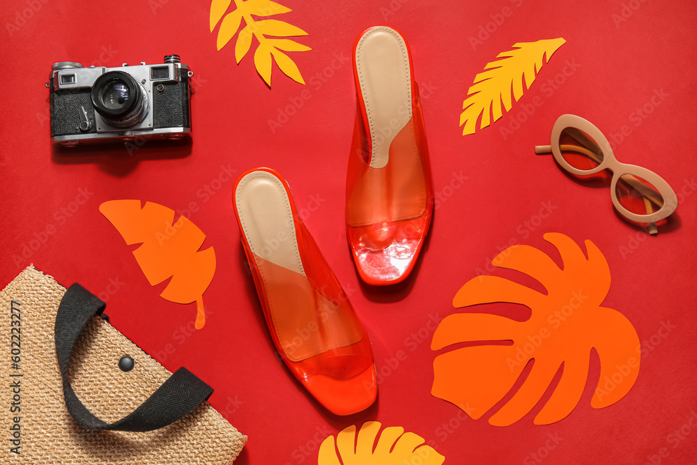 Pair of high heeled sandals with sunglasses, camera and wicker bag on red background