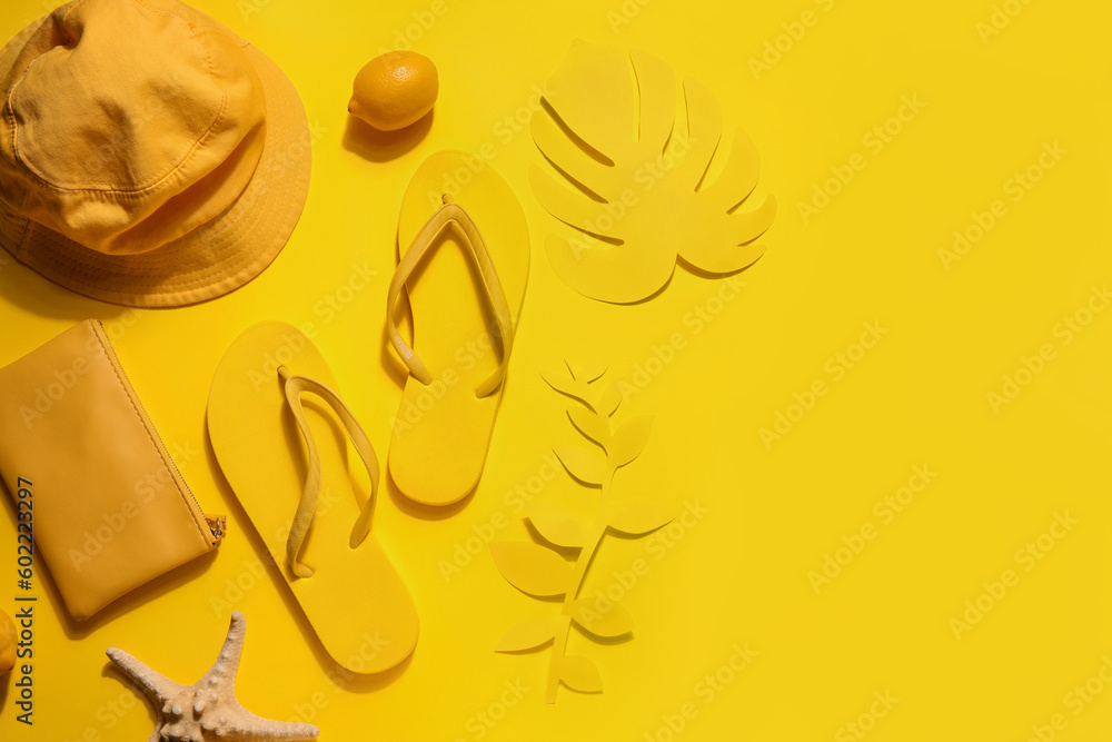 Summer hat with flip flops, bag and palm leaves on yellow background