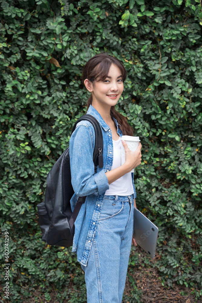 Portrait of young Asian woman student with coffee and backpack outdoor green leaf background