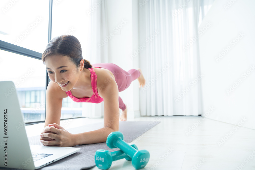 Asian Woman training fitness Plank pose at home watch online tutorial on laptop