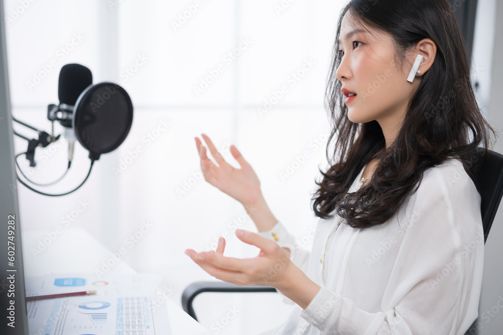 Young Asian woman having online meeting or recording podcast on computer with headphones and microph