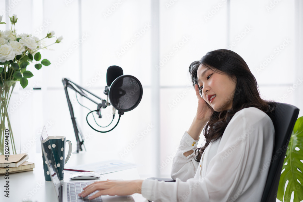 Asian woman working on laptop computer with headphones and microphone at home relaxing and chilling 