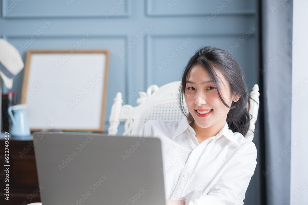 Young asian girl working at a home with a laptop looking at camera.