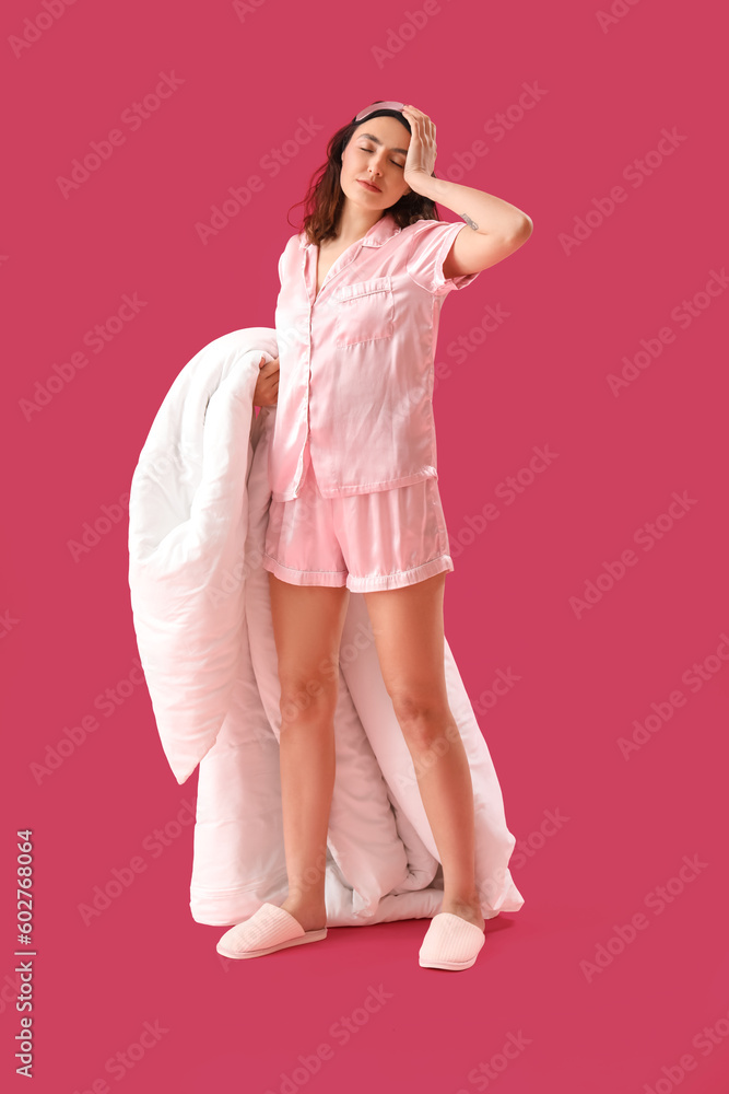 Young brunette woman in pajamas with blanket on pink background