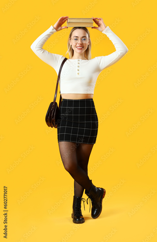 Female student with books on yellow background