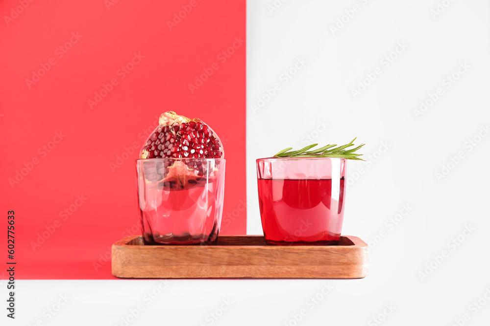 Board with glasses of fresh pomegranate juice on colorful background