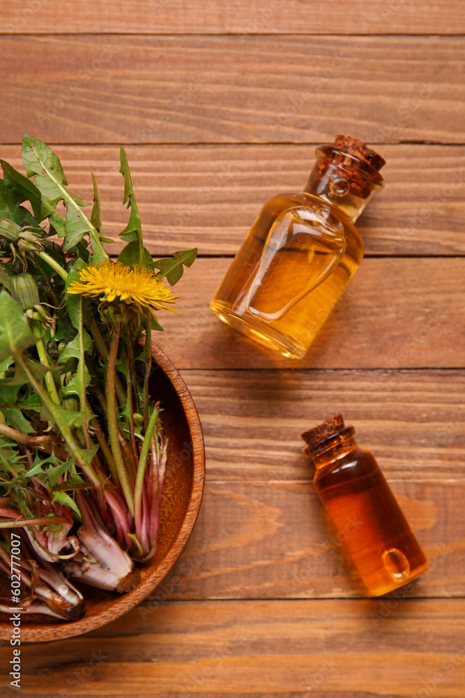 Bottles with cosmetic oil and bowl of dandelion flowers on wooden background