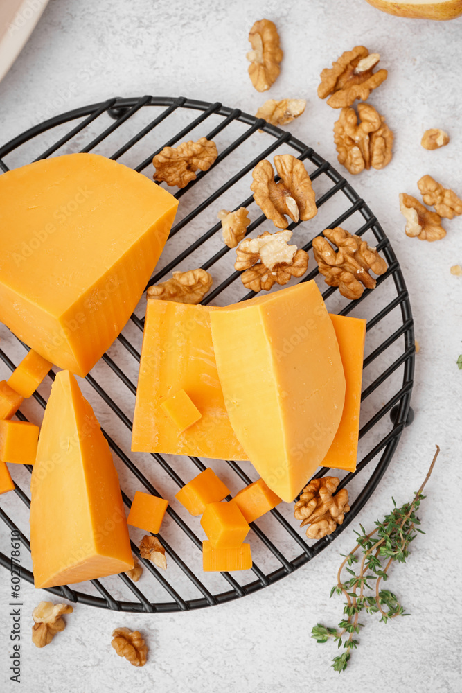 Cooling rack with pieces of tasty cheddar cheese on light background